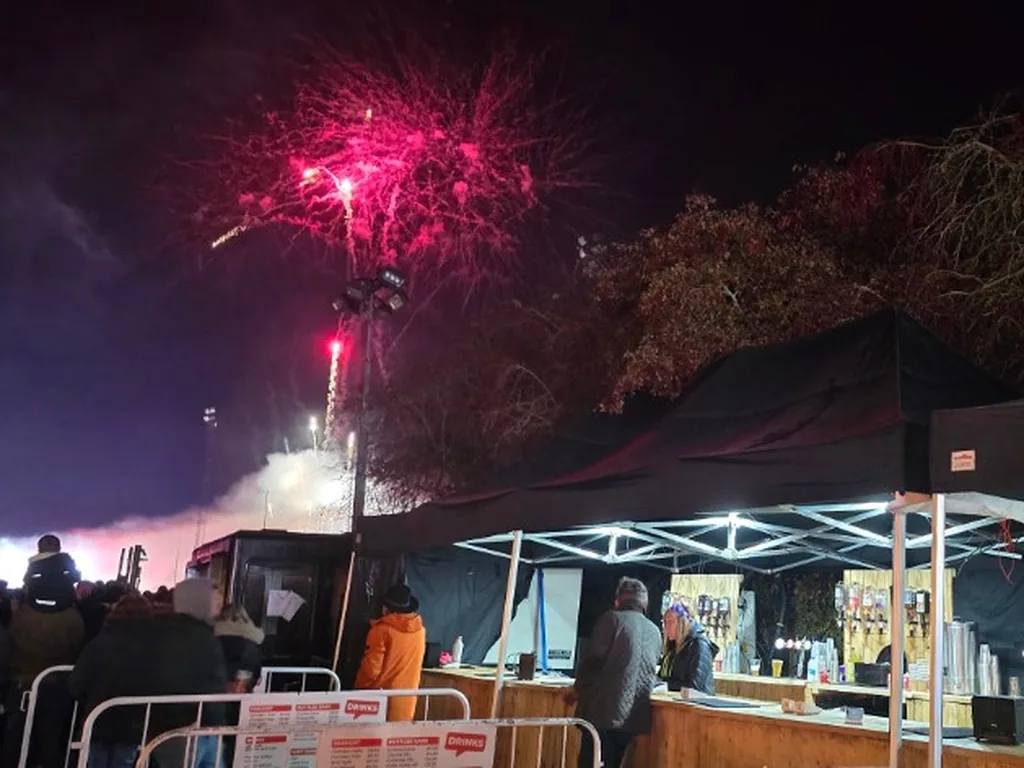 Rustic wooden festival bars under black gazebos at a fireworks night