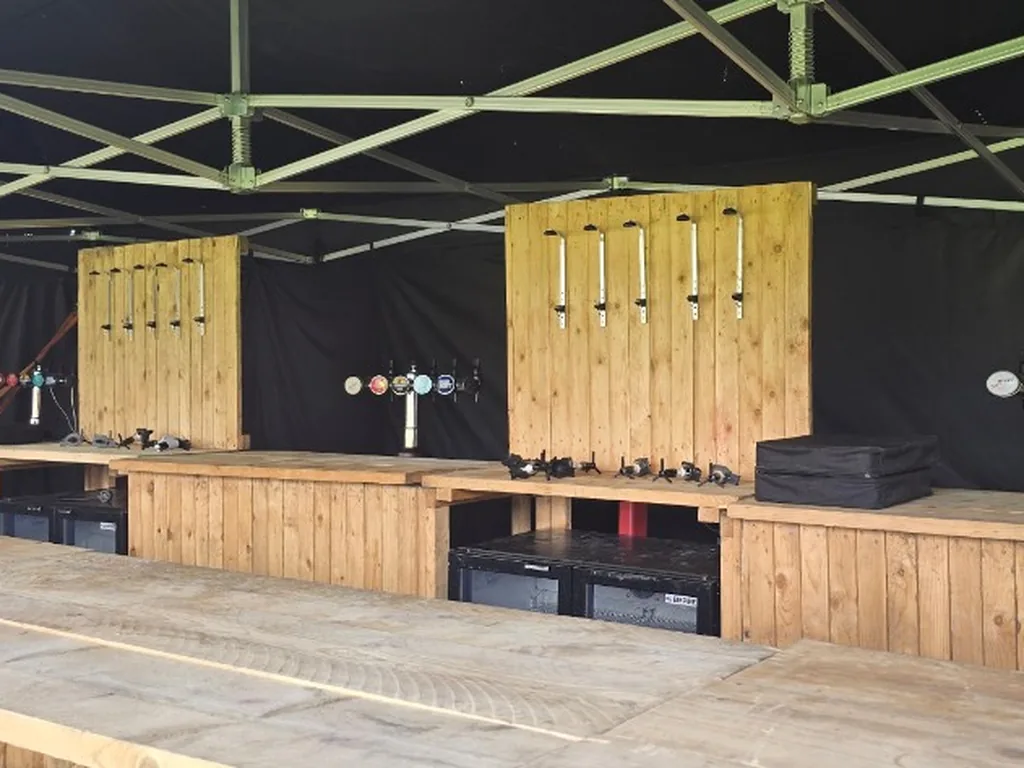 Rustic wooden festival bars and multi-tap fonts under a black marquee at a World Cup fanzone in Bromsgrove