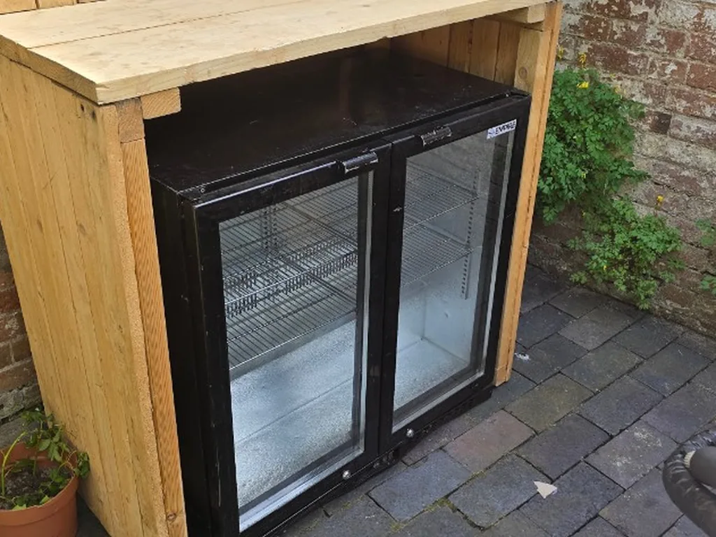 Double-door bottle fridge in a rustic wooden housing in a Warwick courtyard