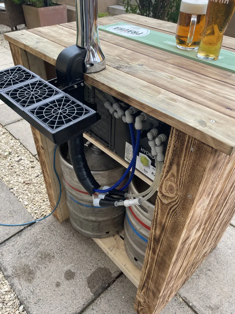 Under-counter view of a keg hire bar: two kegs, a cooler, beer lines and a drip tray, with poured pints on top