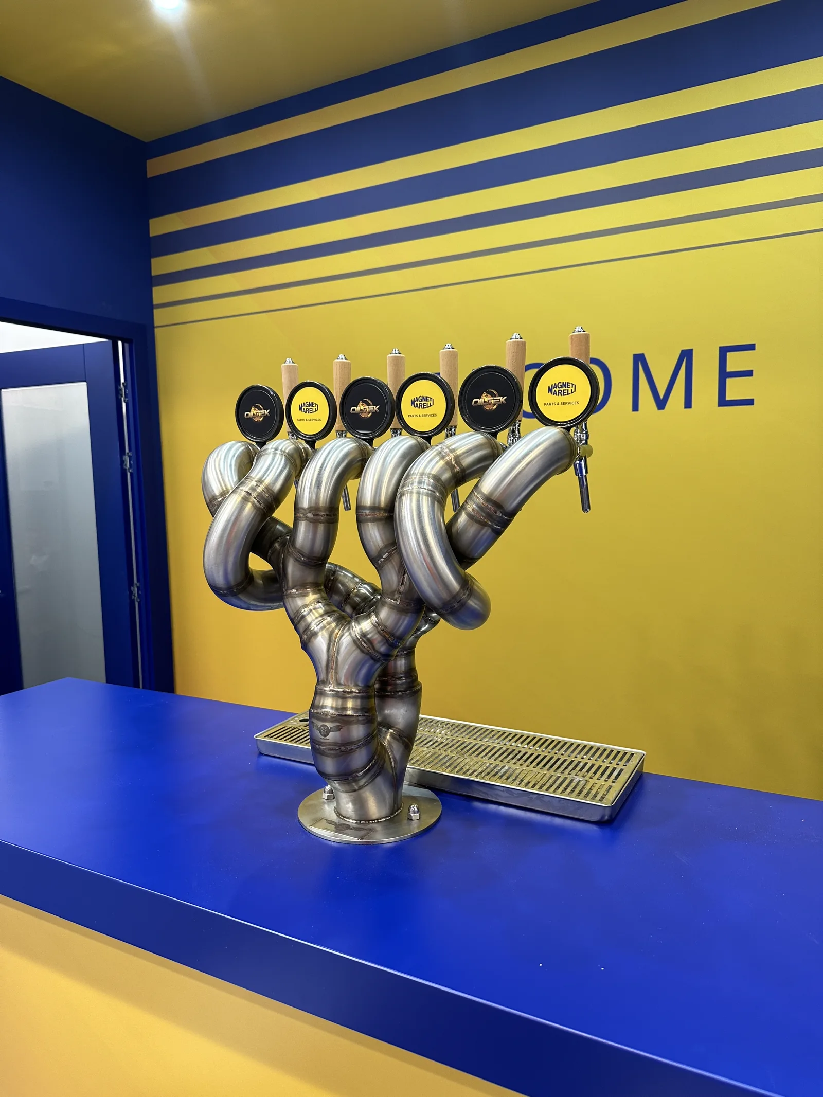 Custom stainless six-tap exhaust-manifold beer font on Magneti Marelli exhibition stand at the NEC Birmingham