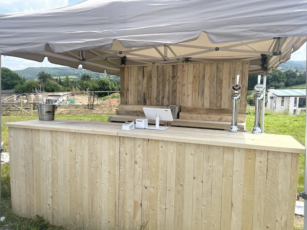 Rustic gazebo bar with a card reader, tablet till, ice bucket and two taps at a field event near Northampton