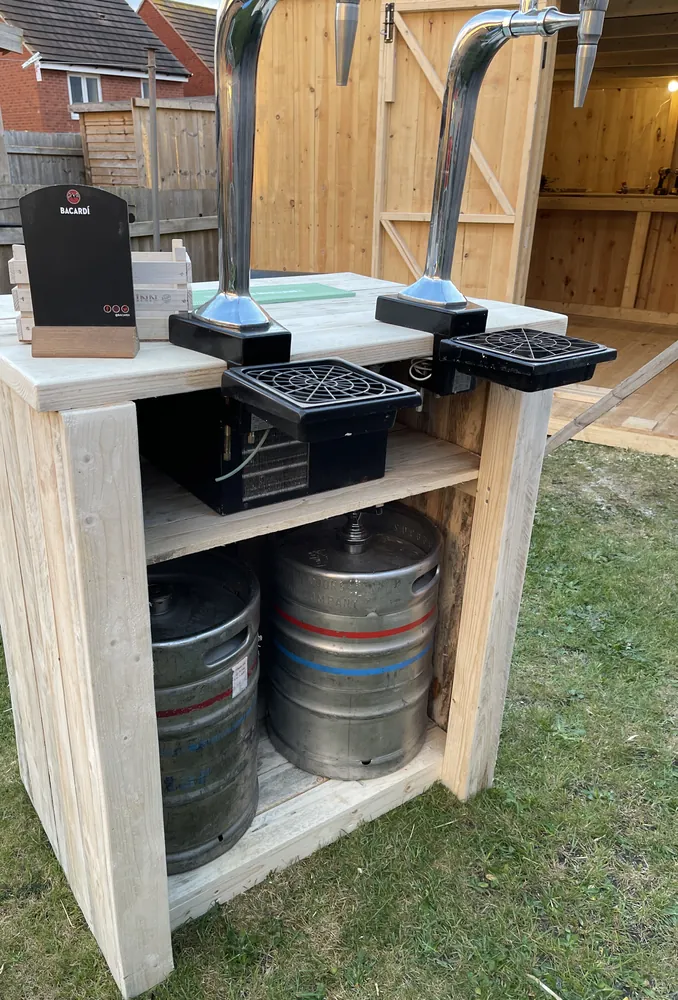 Cooler and two kegs on the shelves under a two-tap rustic garden keg bar